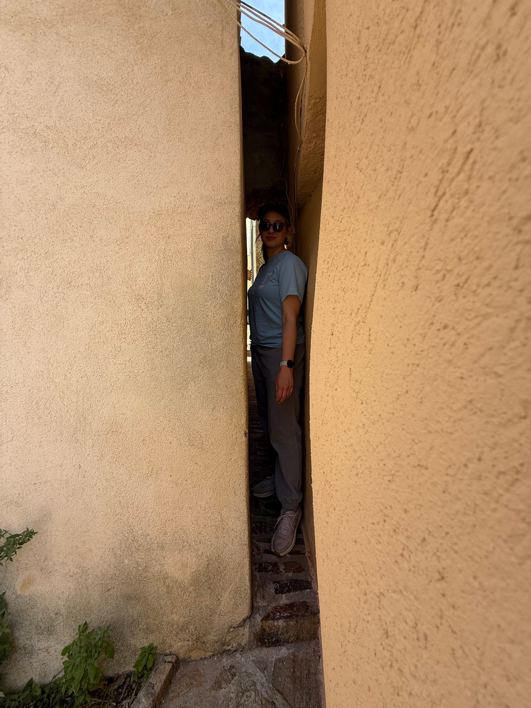 A person standing sideways in a very narrow passage between warm plaster walls